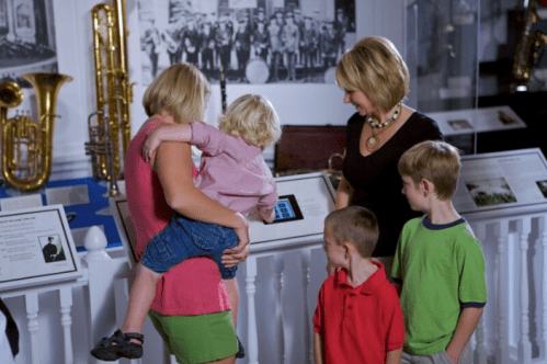 A woman and children explore a museum exhibit featuring musical instruments and historical displays.