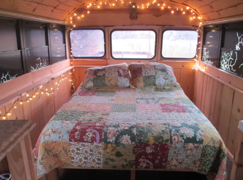 Cozy interior of a bus converted into a living space, featuring a bed with a patchwork quilt and string lights.