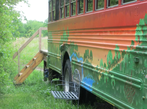 A colorful, painted bus parked in a grassy area with wooden steps leading up to it.