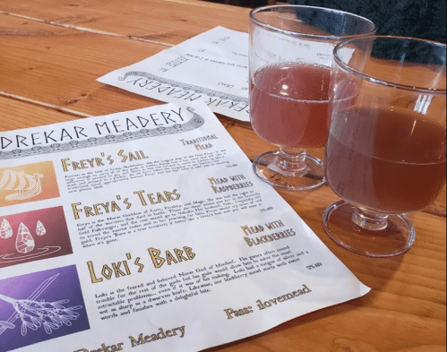Two glasses of mead with a menu from Drekar Meadery featuring various mead options on a wooden table.