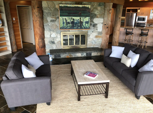 Cozy living room with gray sofas, a coffee table, and a stone fireplace, featuring a colorful artwork on the wall.