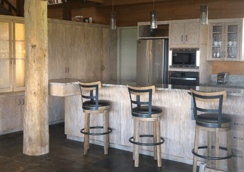 Modern kitchen with wooden cabinets, a large island, and three bar stools, featuring stainless steel appliances.
