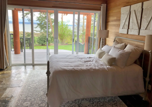 Cozy bedroom with a large bed, wooden walls, and sliding glass doors opening to a scenic outdoor view.