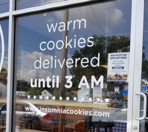 Sign on a store window advertising warm cookie delivery until 3 AM from Insomnia Cookies.