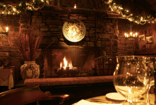 Cozy restaurant interior with a stone fireplace, warm lighting, and festive decorations, creating an inviting atmosphere.