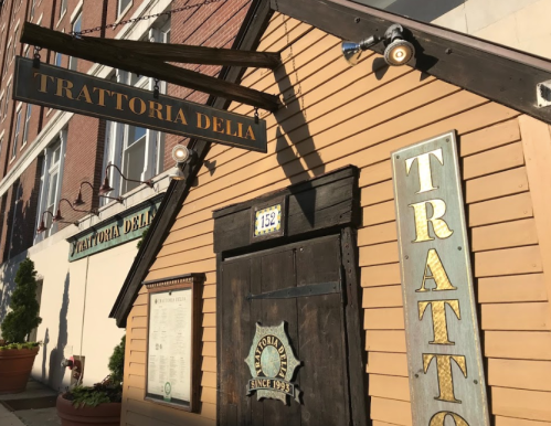 Exterior of Trattoria Delia, featuring a wooden sign and a door with a decorative emblem, set against a brick building.