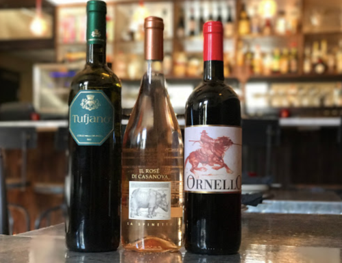 Three wine bottles on a bar: a green bottle labeled Tufjano, a pink bottle labeled Il Rosé di Casanova, and a red bottle labeled Ornello.