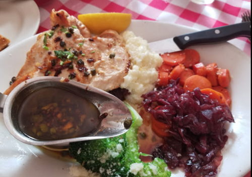 A plate of food featuring grilled chicken, mashed potatoes, broccoli, carrots, and red cabbage with a sauce on the side.