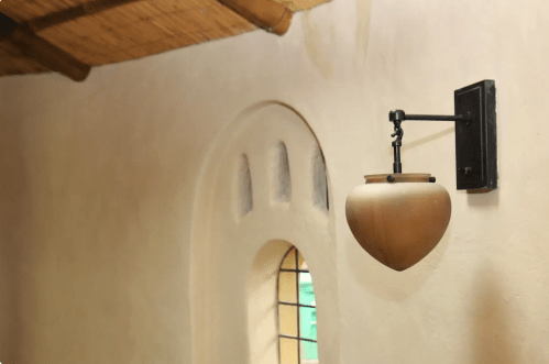 A wooden pot hangs on a black wall mount beside a curved window in a rustic interior.