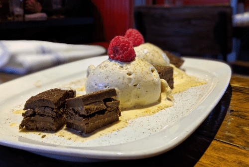 A dessert plate featuring two scoops of vanilla ice cream, chocolate layers, and topped with raspberries.