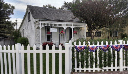 A quaint white house with a porch, surrounded by a white picket fence and decorated with red, white, and blue bunting.