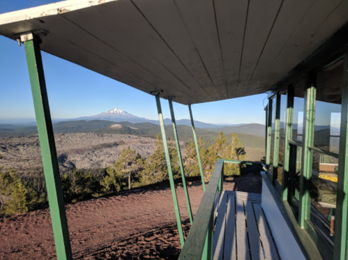 View from a lookout tower, featuring a mountain in the distance and a forested landscape under a clear sky.