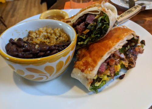 A plate with two burritos filled with meat and vegetables, alongside a bowl of black beans and rice.