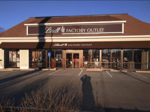 Exterior of a Lindt Factory Outlet store with a clear blue sky and a shadow in the foreground.