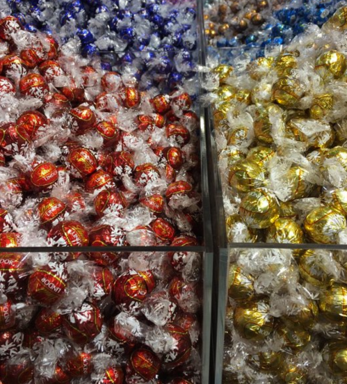 A display of colorful wrapped chocolates in red, gold, and blue, arranged in clear containers.