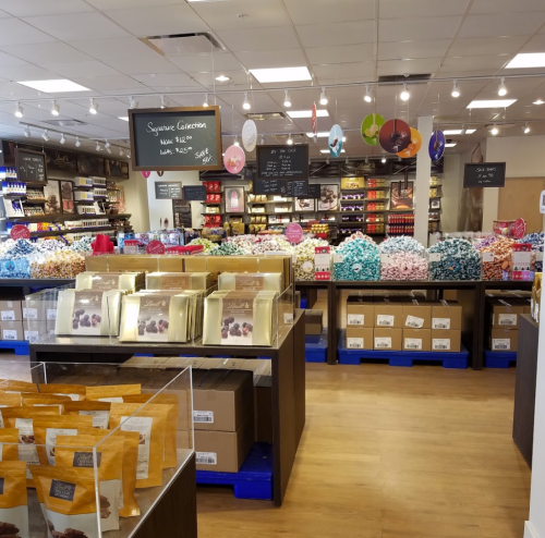 A colorful candy store interior with shelves filled with various sweets and treats, and display tables in the foreground.