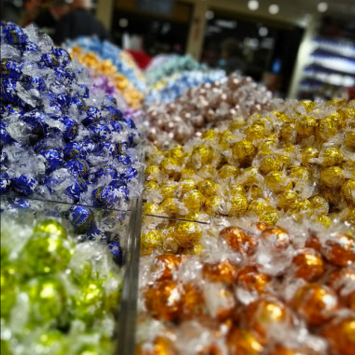 A colorful display of wrapped chocolates in various shades, arranged in a market setting.