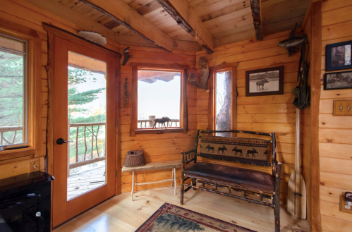 Cozy wooden interior of a cabin with large windows, a rustic bench, and decorative items on the walls.