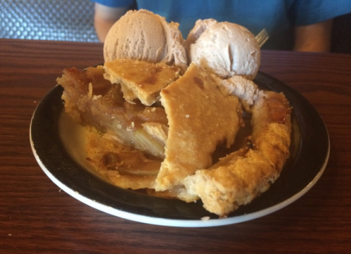 A slice of apple pie topped with two scoops of chocolate ice cream on a black plate.