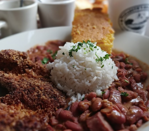 A plate of rice topped with parsley, served with red beans, cornbread, and crispy fried chicken.