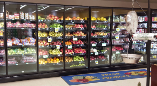 A grocery store produce section with colorful fruits displayed on shelves, including apples, oranges, and pineapples.
