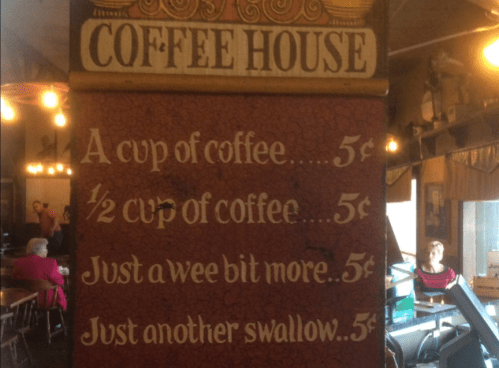 Sign in a coffee house listing prices: A cup of coffee 5¢, ½ cup 5¢, Just a wee bit more 5¢, Just another swallow 5¢.