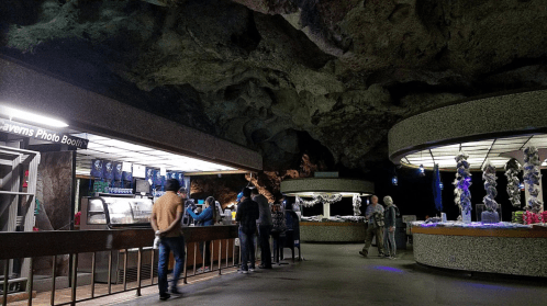 Interior of a cave-like space with visitors at a photo booth and a gift shop, featuring rocky ceilings and unique decor.