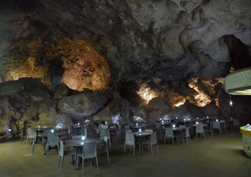 A unique restaurant inside a cave, featuring stone walls, tables, and soft lighting for a cozy atmosphere.