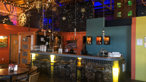 A vibrant café interior featuring a colorful bar, decorative lights, and a cozy seating area.