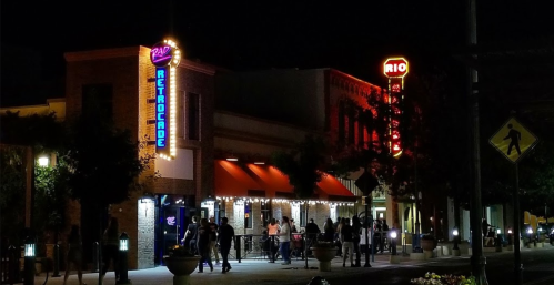 A lively night scene of a retro arcade and a bar, with colorful neon signs and people walking outside.