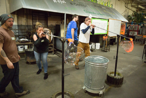 A group of people working together to create glass art in a studio, using glassblowing techniques.