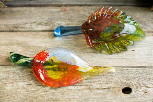 Two colorful glass sculptures resembling a fish and a leaf, resting on a rustic wooden surface.