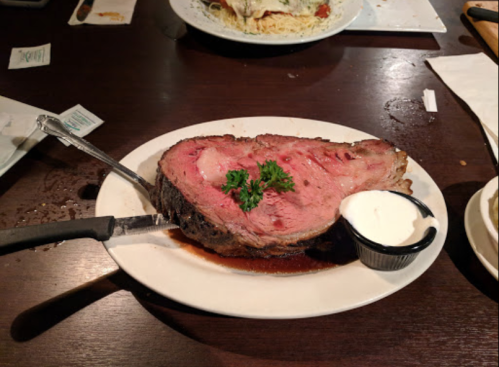 A large slice of prime rib on a plate, garnished with parsley, accompanied by a small bowl of creamy sauce.