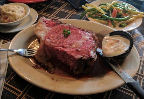 A plate featuring a large slice of prime rib with a side of green beans and mashed potatoes.