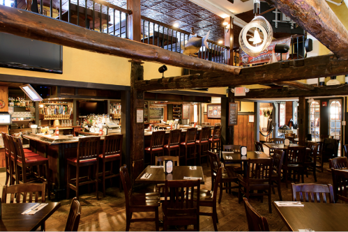 Cozy restaurant interior with wooden beams, a bar, and tables set for dining. Warm lighting creates an inviting atmosphere.
