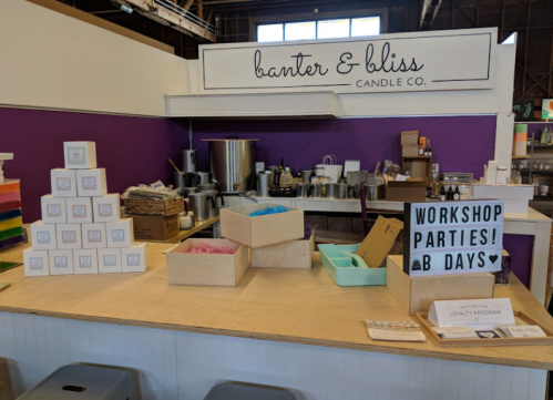 A candle shop display featuring colorful wax, boxes, and a sign promoting workshops and parties.
