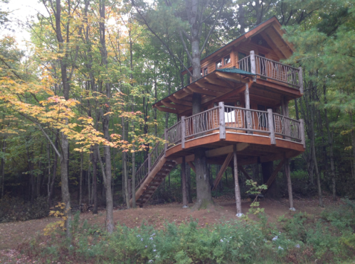 A wooden treehouse with a balcony, nestled among colorful autumn trees in a forest.