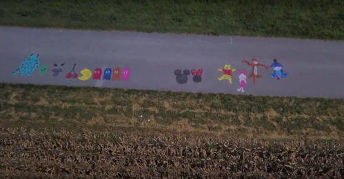Colorful chalk drawings of characters and shapes on a pathway, surrounded by grass and a field.
