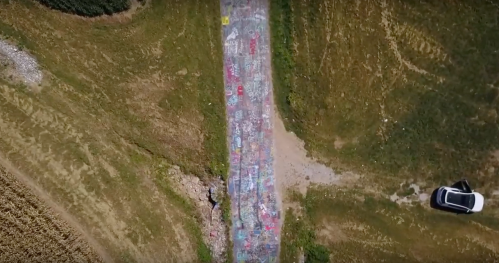 Aerial view of a colorful graffiti-covered path surrounded by green fields and rocky terrain.