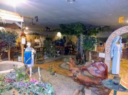 A whimsical indoor scene featuring sculptures, greenery, and a pathway, creating a serene, artistic environment.