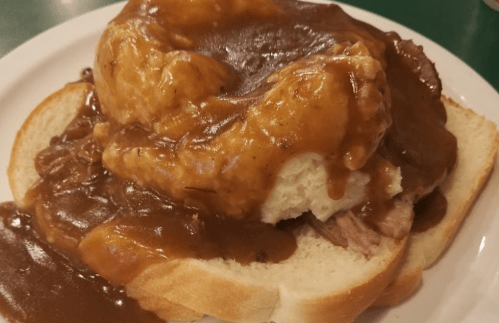 A plate of bread topped with mashed potatoes, beef, and brown gravy.