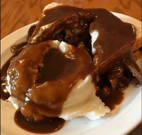 A plate of mashed potatoes topped with gravy, alongside slices of bread and tender beef covered in brown sauce.