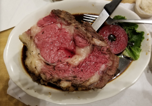 A large, juicy prime rib served on a plate with a side of lettuce and a slice of red gelatin dessert.