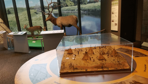 A museum display featuring a diorama of Native American life, with models of tents and taxidermy deer and elk.