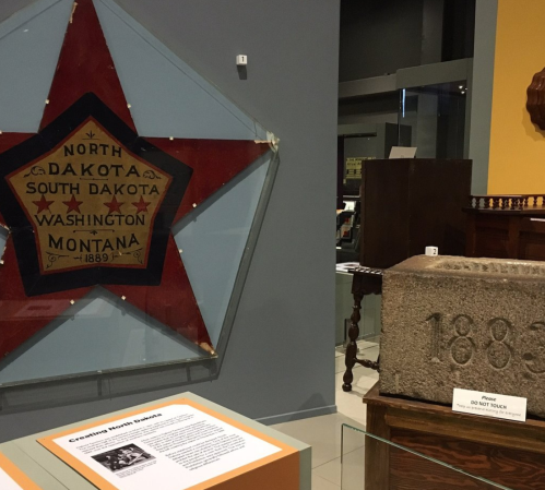 A museum display featuring a star-shaped banner for North Dakota and a stone block marked "1883."