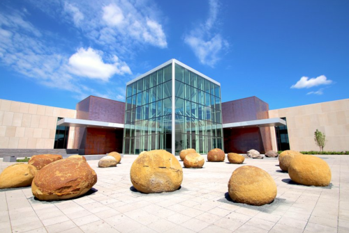 Modern glass building surrounded by large, smooth boulders on a sunny day with blue skies and scattered clouds.