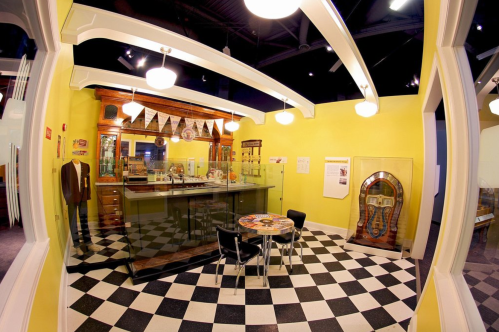 A retro diner interior featuring a checkered floor, bar counter, jukebox, and vintage decor.