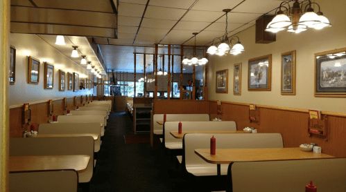 A cozy diner interior with booths, tables, and framed pictures on the walls, illuminated by hanging lights.
