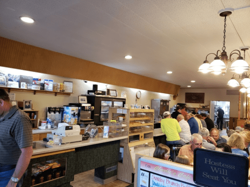 A busy café interior with customers seated at tables and a counter displaying baked goods and drinks.