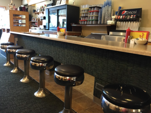A diner counter with chrome stools, condiments, and a drink dispenser in a cozy, casual setting.